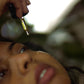 A close-up lifestyle shot of a person holding a dropper of SIORA luxury Oil bottle above their face, with a gold dropper containing golden oil hovering near their eye.