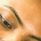 Close-up of a person's eye and eyebrow area, showing natural skin texture and dark brown eyebrow with SIORA Luxury Oil.